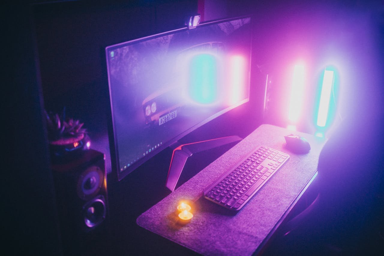 A stylish gaming desk featuring neon lights, keyboard, and monitor in a dark room.