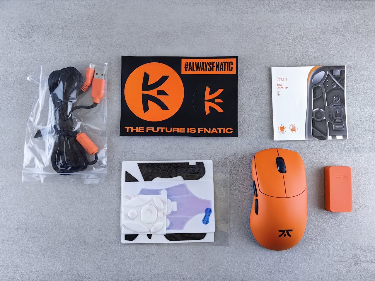 Flat lay of Fnatic gaming mouse, accessories, and branding materials on a gray surface.